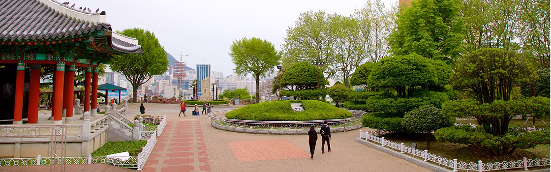 Um parque da cidade de Busan, cheio de grama verde, um templo e pessoas passeando.